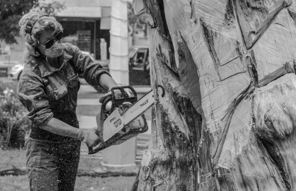 Grayscale Photo of a Person Trimming a Tree Log